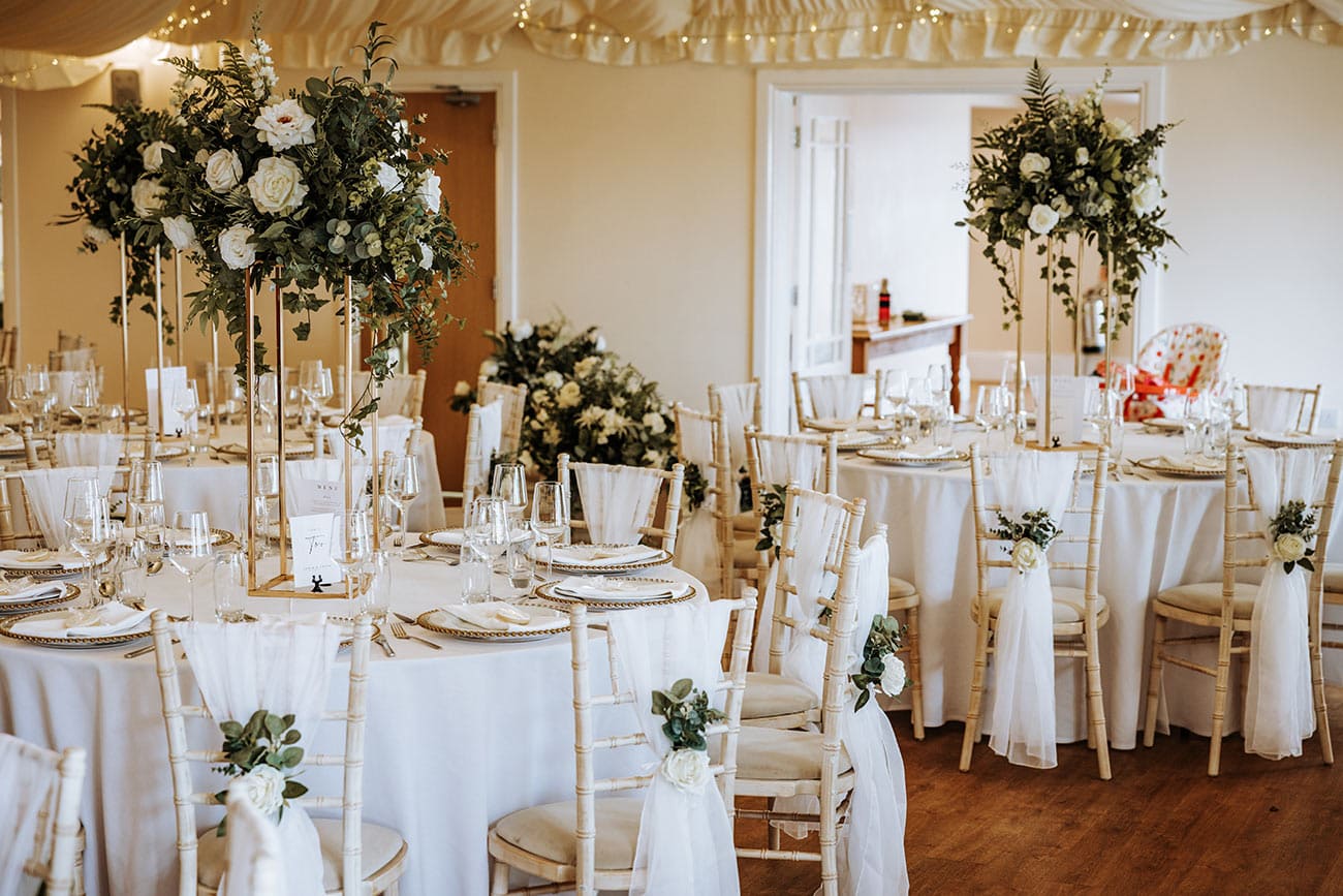 The reception room set up with white clothed tables and floral displays