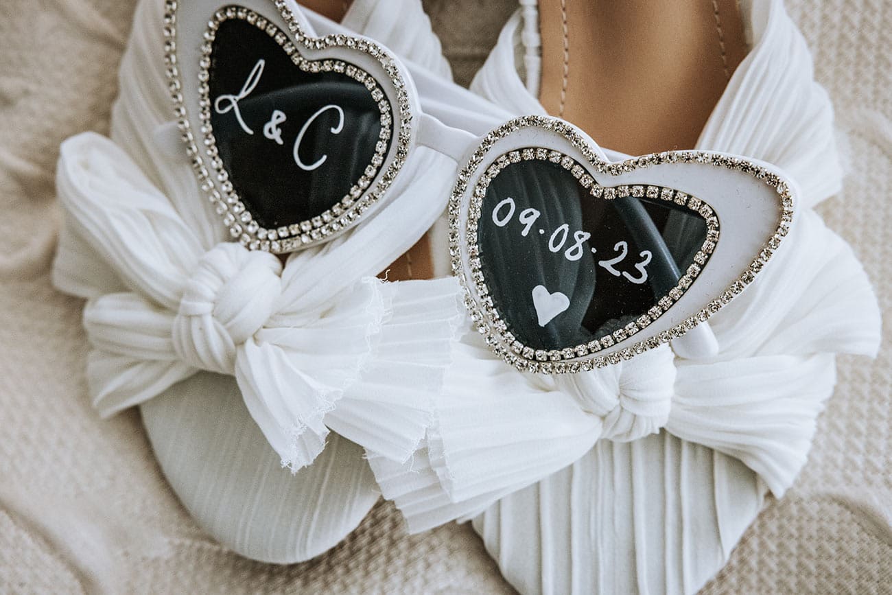 Bride's white bridal shoes with personalised heart detailing with the bride and groom's initials and the date of the wedding on them