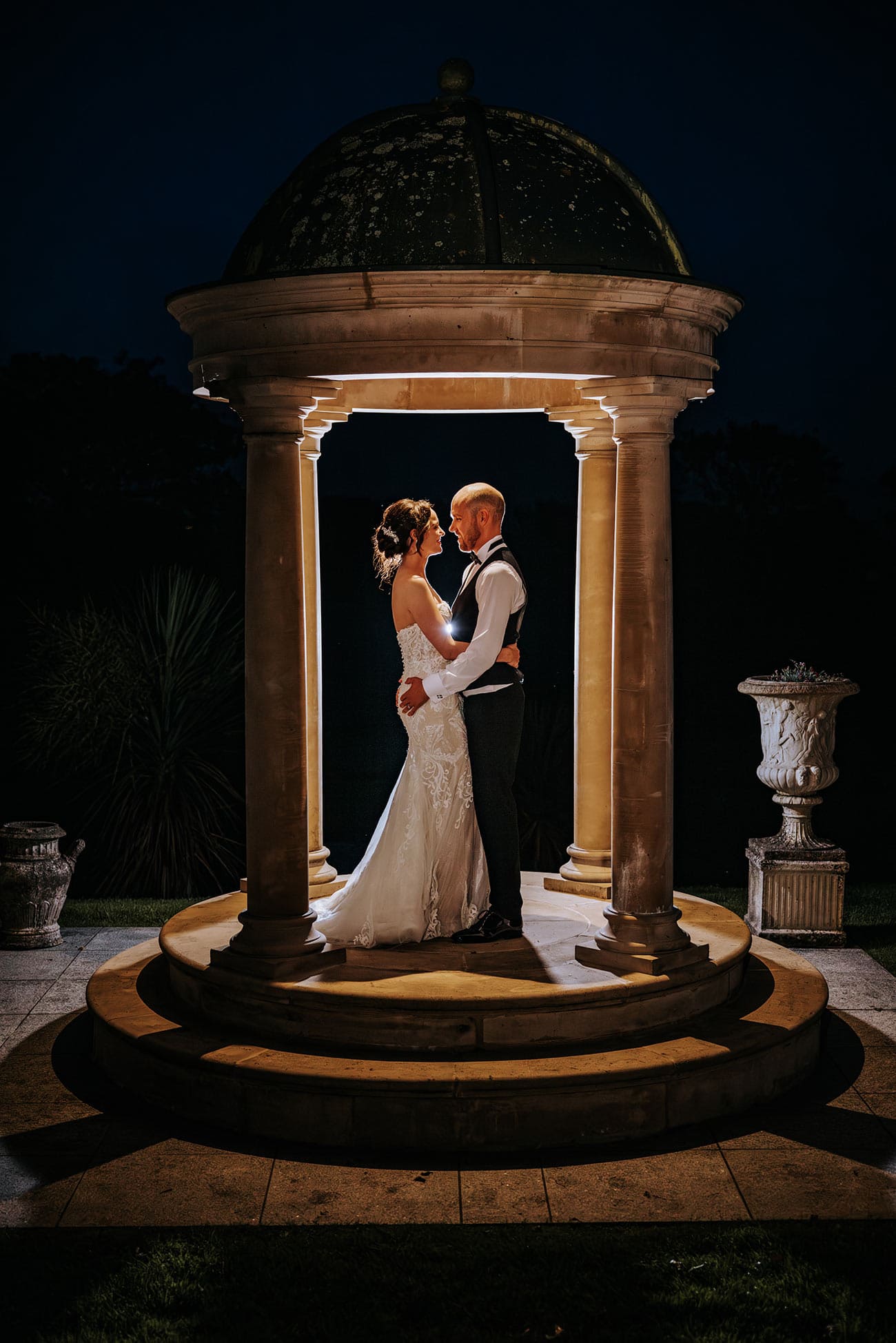 bride and groom embracing under a lit up arch