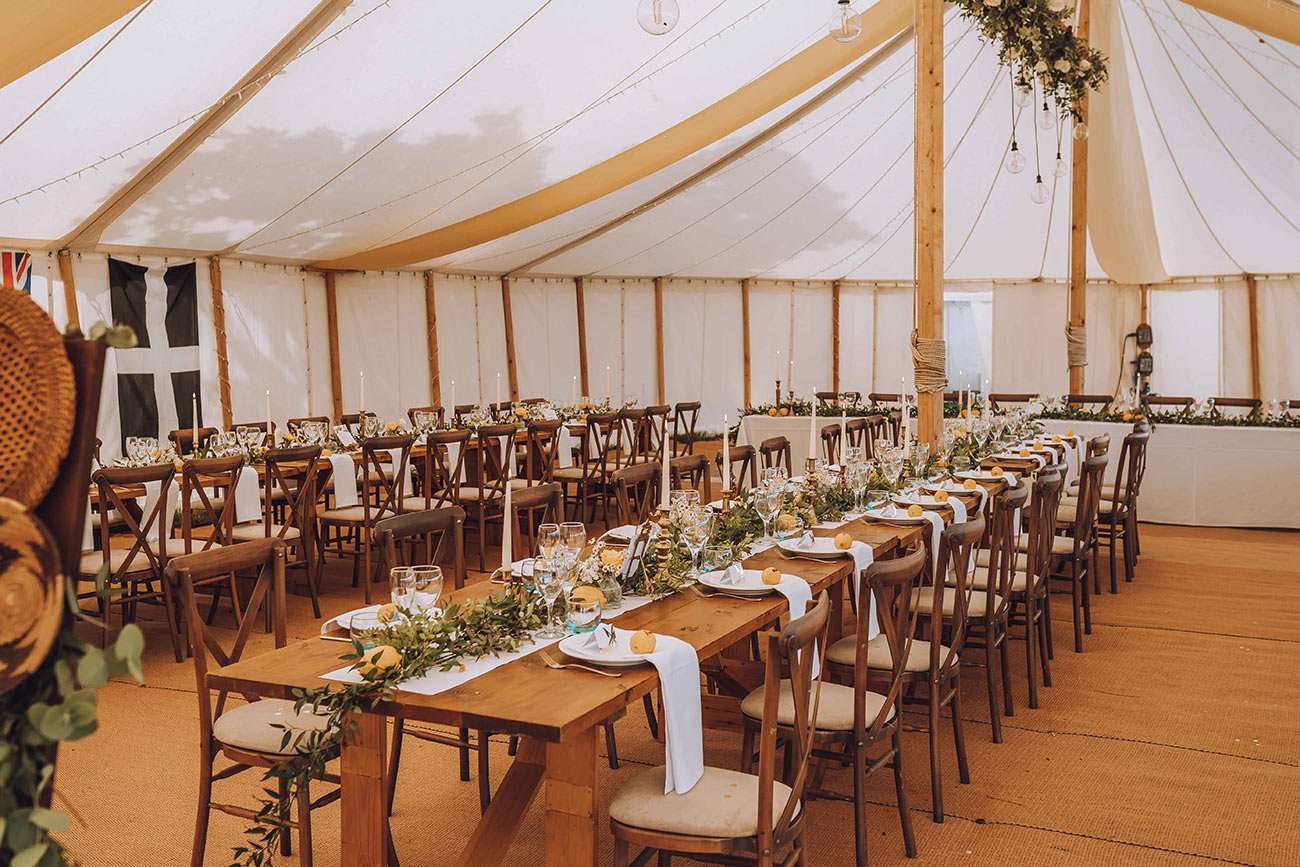 The marquee laid up for the reception with wooden chairs and trestle tables with a colour scheme of yellow 