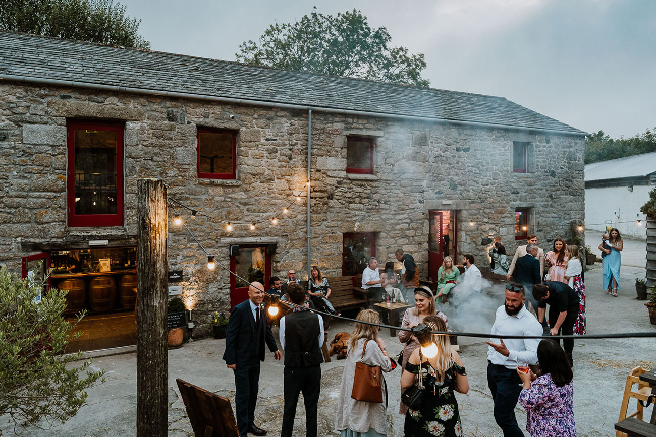 Wedding guests outside a rustic barn having drinks and chatting