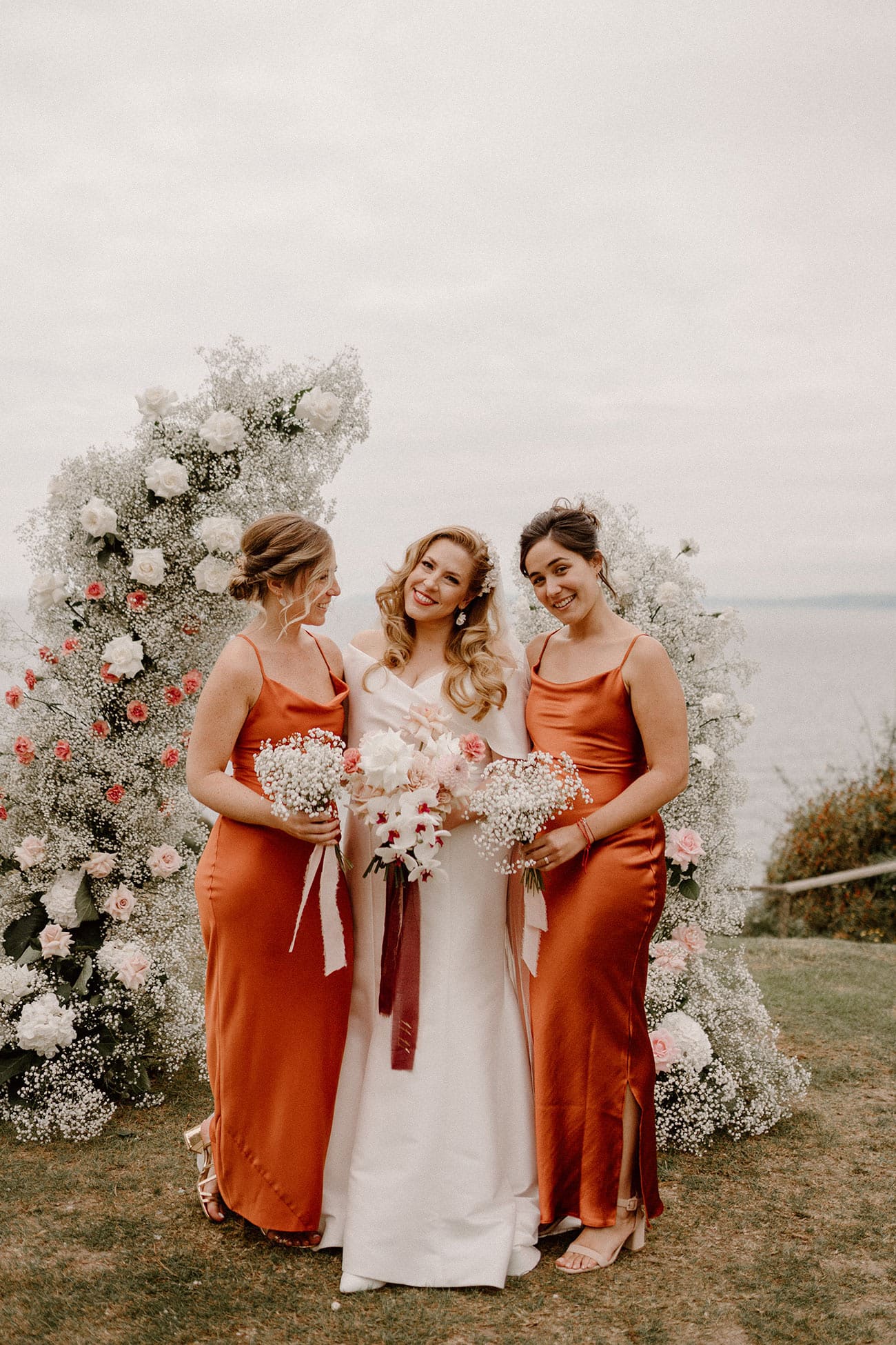 The bride posing with her two bridesmaids who are in copper dresses