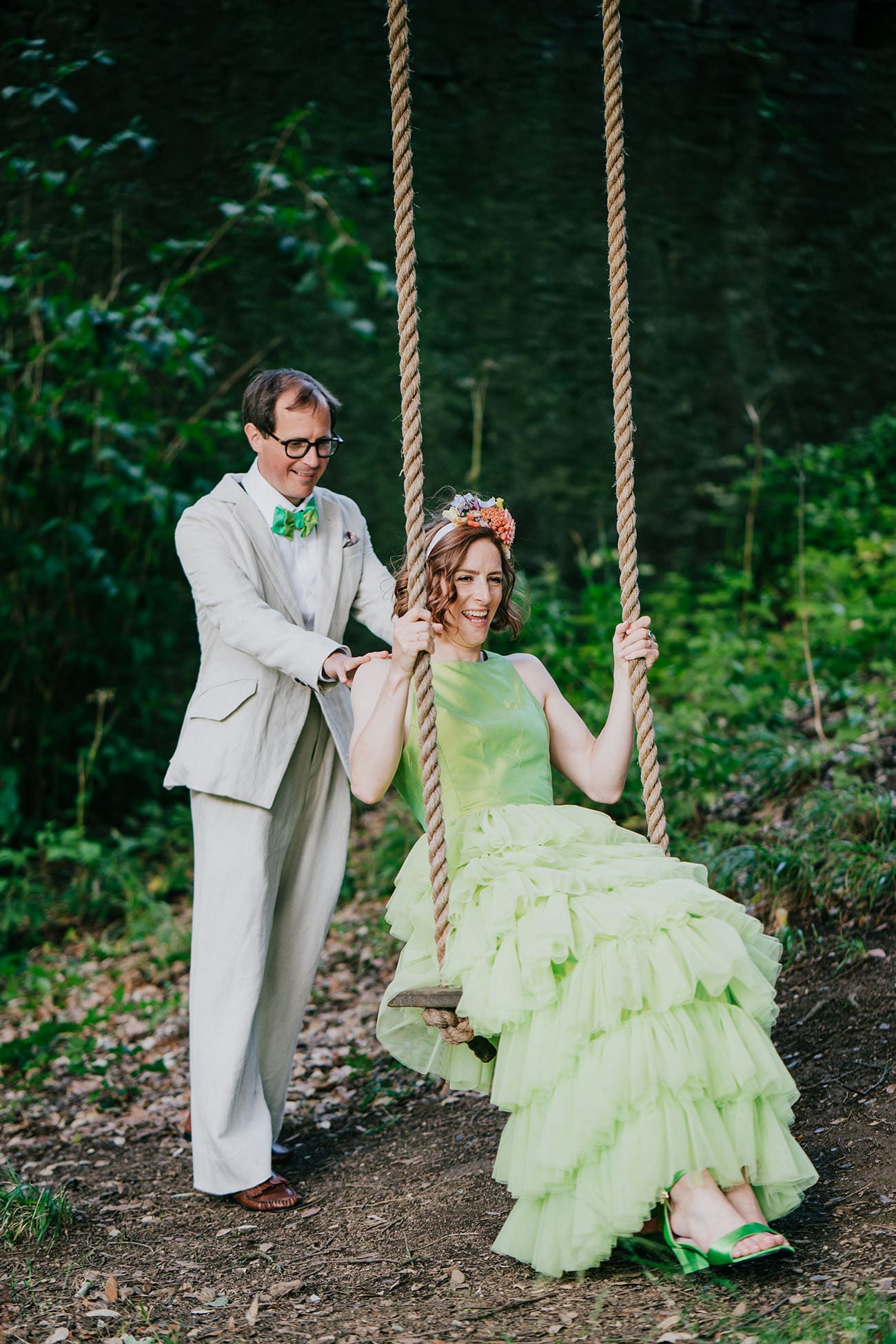 The groom pushes his smiling wife on a tree swing