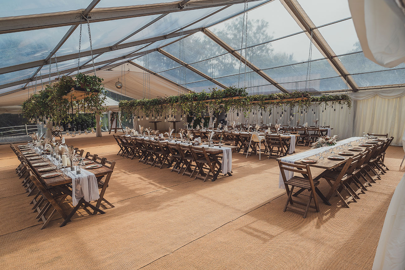 Wedding reception in marquee with wooden trestle tables, wooden chair and floral arch